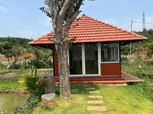 una pequeña casa roja con un árbol delante en Dak Nguyen Homestay & Farm 2, en Gia Nghĩa