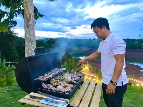 a man is cooking meat on a grill at Dak Nguyen Homestay & Farm 3 in Gia Nghĩa