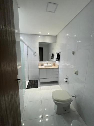 a white bathroom with a toilet and a sink at Casa com quarto disponível em Guaramirim in Guaramirim