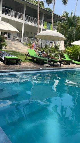 a pool with chairs and an umbrella next to a hotel at Plantation House in Hikkaduwa