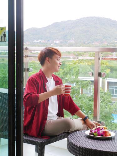 a young man sitting on a balcony holding a cup of coffee at Amari Hua Hin in Hua Hin