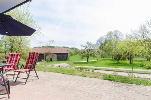 zwei rote Stühle und ein Regenschirm auf einer Terrasse in der Unterkunft Ferienwohnung Kobelsberg in Aufseß