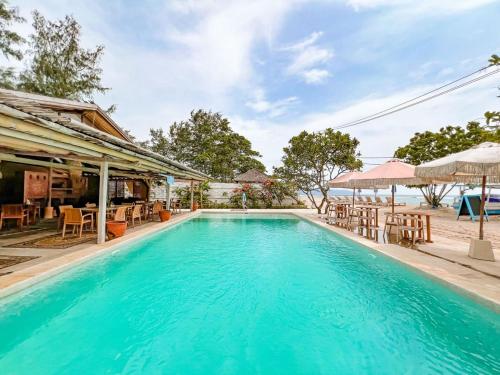 a swimming pool with tables and chairs next to a house at Bungalow Cafe Gili Beachfront in Gili Meno