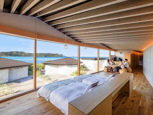 ein großes Bett in einem Zimmer mit großen Fenstern in der Unterkunft Denpaku The Beachfront MIJORA in Amami