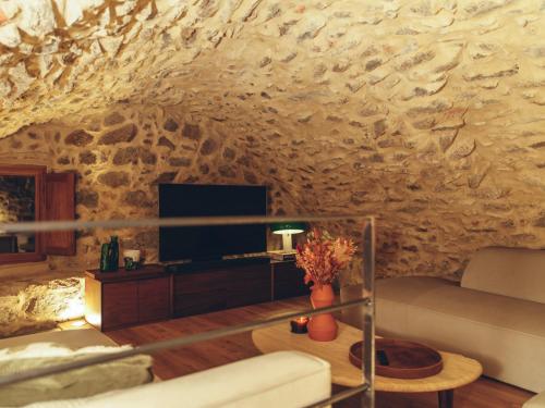 sala de estar con pared de piedra, sofá y TV en La Grotte, en Corbara