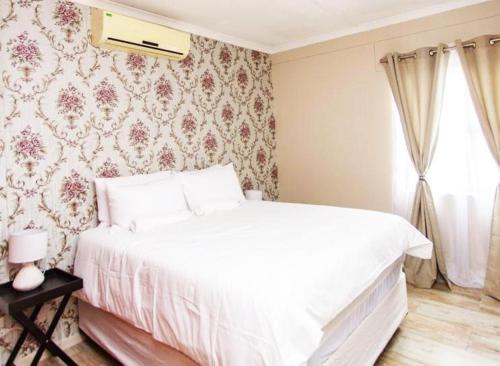 MorningSide Fortyfive في Ongwediva: سرير أبيض في غرفة نوم مع ورق جدران زجاجي