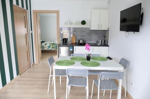 a kitchen with a white table with chairs and a pink flower at Apartamenty Poddąbek- basen kryty, sauna, animacje dla dzieci , małpi gaj, baseny na dachu in Poddąbie