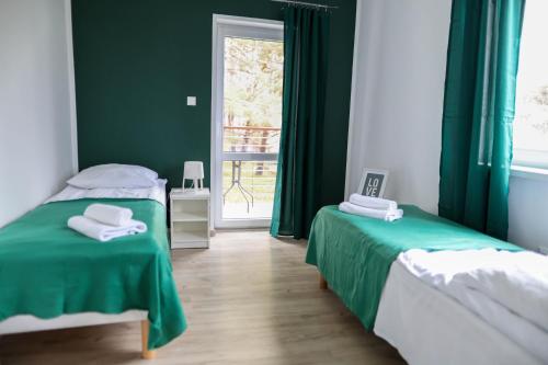 two beds in a room with green curtains and a window at Apartamenty Poddąbek- basen kryty, sauna, animacje dla dzieci , małpi gaj, baseny na dachu in Poddąbie