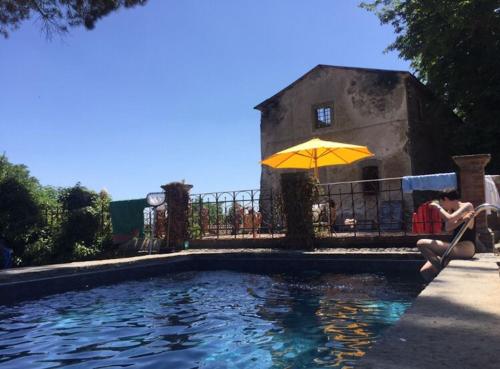 a woman sitting under an umbrella next to a swimming pool at Appartamenti Lais in Sipicciano in Sipicciano