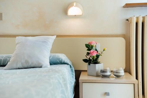 Una cama con una almohada y un jarrón de flores en una mesita de noche en Hotel Atlantic en Loano