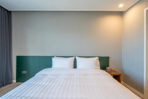 a bedroom with a large white bed with a green headboard at Chestertons Naksan in Yangyang