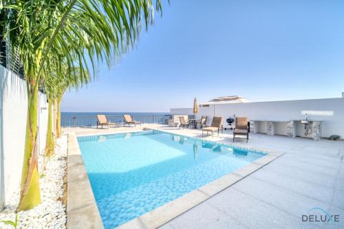 a swimming pool with palm trees and the ocean at Dazzling 4BR Villa with Assistant’s Room at Al Dana Villa Sharm, Fujairah by Deluxe Holiday Homes in Fujairah