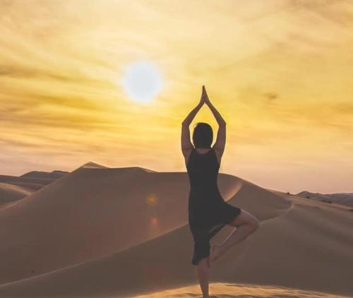 a woman performing a yoga pose in the desert at Aladdin Merzouga Camp in Merzouga