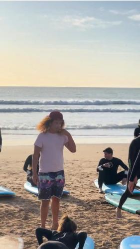 a woman standing on a beach with people on surfboards at Lunja Village - Agadir in Taghazout
