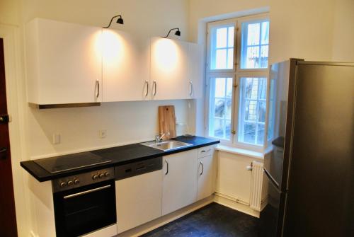 a kitchen with white cabinets and a sink and a refrigerator at Aparthotel Mageløs 12 in Odense