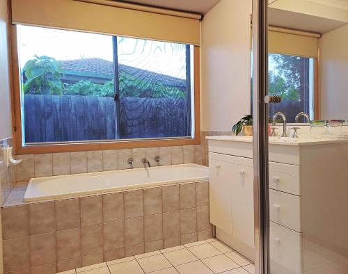 baño con bañera, lavabo y ventana en YF Hostel, en Craigieburn