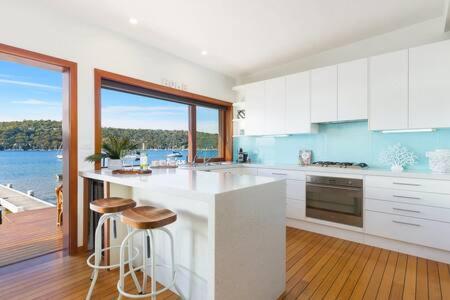 une cuisine avec des armoires blanches et une vue sur l'eau dans l'établissement Waterfront Scotland Island Holiday Home - Family & Pet Friendly - 3 Bedrooms - Wifi - Netflix - Private Jetty, à Scotland Island