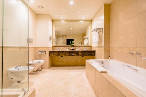 a bathroom with a tub and a toilet and a sink at Southern Sun Sandton in Johannesburg
