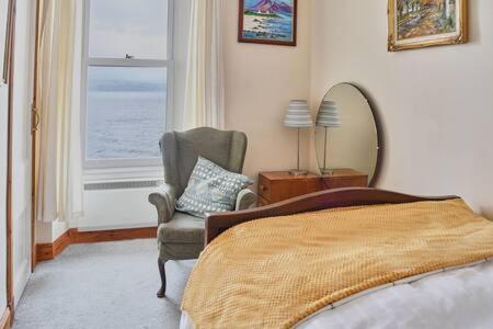 1 dormitorio con cama, silla y espejo en Host & Stay - Freshwater River View, en Dunoon