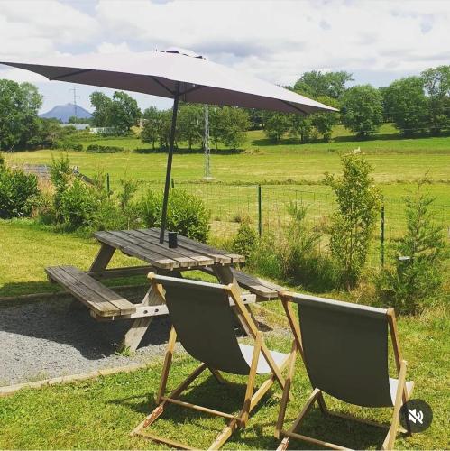 - une table de pique-nique et 2 chaises avec un parasol dans l'établissement Logement insolite au cœur de l'Auvergne, à Rochefort-Montagne