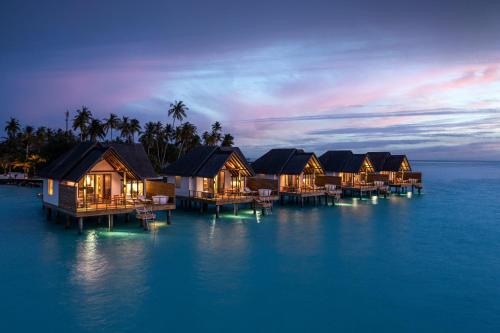 a group of houses on the water at night at Fushifaru Maldives with 50 percent off on sea plane roundtrip 04 nights & above in Fushifaru