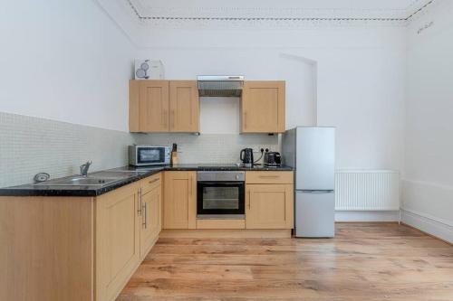 a kitchen with wooden cabinets and a white refrigerator at Central Muswell Hill- One Bed in London
