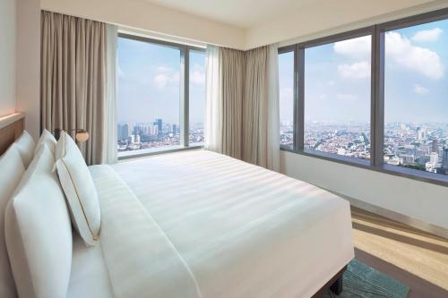 a bedroom with a large white bed with large windows at PARKROYAL Serviced Suites Jakarta in Jakarta