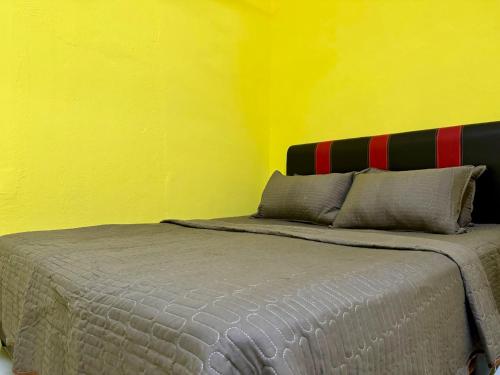 - une chambre dotée d'un lit avec un mur jaune dans l'établissement Teratak Tok Ma Rumah Nyatuh, à Kampong Wakaf Tengah