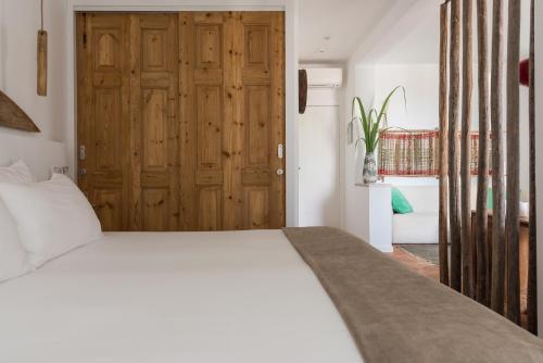 a bedroom with a white bed and a wooden door at Altanure Almatere - Food Forest Boutique Stay in Tavira