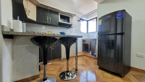 eine Küche mit einem schwarzen Kühlschrank und schwarzen Barhockern in der Unterkunft apartamento banderas 2 in Pereira