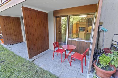 a patio with red chairs and a table and a window at Magnifique studio avec terrasse au centre in Crans-Montana
