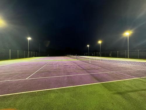 a tennis court at night with lights on it at ShowHomes in Broughton