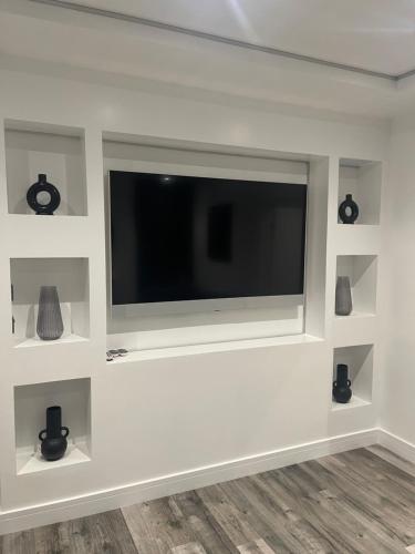 a flat screen tv on a white wall with shelves at DULEX ROOMS in Scunthorpe