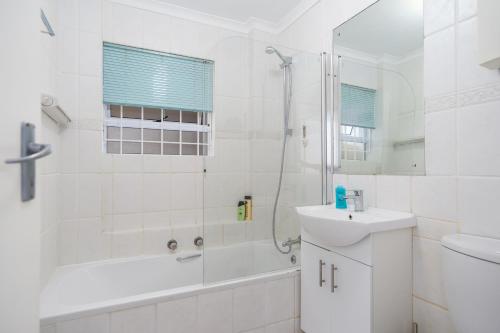 ein weißes Bad mit einer Dusche und einem Waschbecken in der Unterkunft Tranquil Haven with Uninterrupted Power, a Serene Oasis in the Heart of Cape Town in Kapstadt
