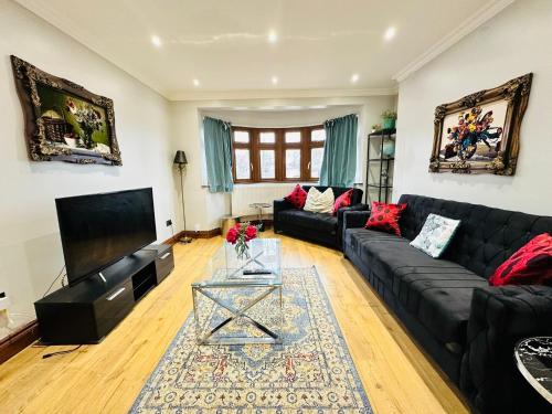 a living room with a black couch and a tv at Spacious 6 Bed Residence in Wembly, London in London
