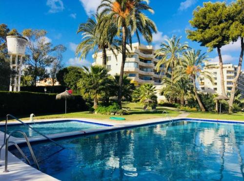 ein Swimmingpool mit Palmen und einem Gebäude in der Unterkunft Habitación deluxe con baño privado en Atalaya Apartagolf, Estepona in Estepona