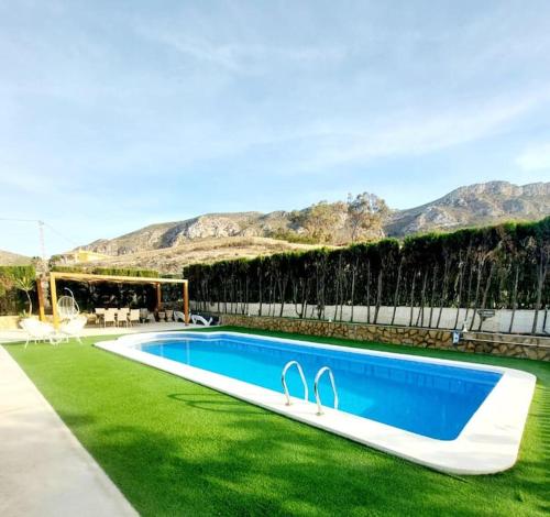 a swimming pool in the middle of a lawn with mountains at Villa Del Cabo in Águilas