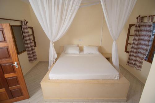 1 dormitorio con 1 cama con sábanas y cortinas blancas en Watamu GK Palms en Watamu