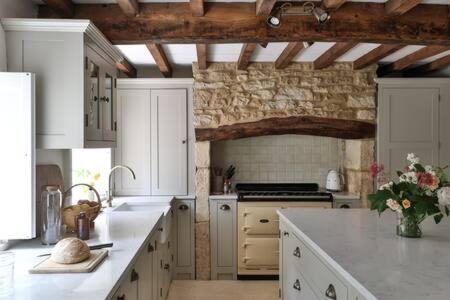 a kitchen with white cabinets and a stone wall at Two Rose Walk Cottage Cotswolds in Moreton in Marsh
