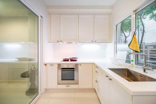 d'une cuisine avec des placards blancs, un évier et une fenêtre. dans l'établissement MIQ_home403/Asok BTS/Resort Pool/9pax/1000MbWifi, à Klong Toi