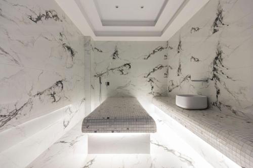 a white bathroom with a bench and a sink at Destiny Hotel & SPA in Tirana