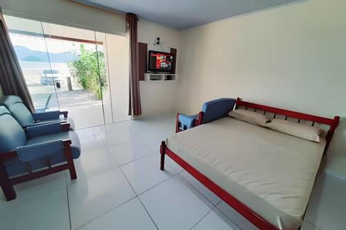 a bedroom with a bed and a chair and a tv at Frente ao mar casa 42 Praia do Estaleiro in Ubatuba