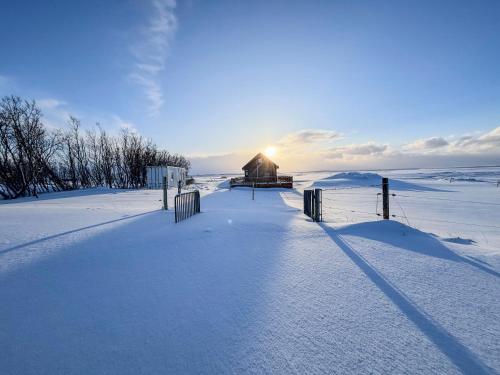 a barn in a snow covered field with the sun setting at Áshamrar in Hella