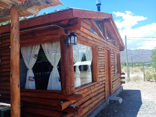 a wooden cabin with a window with white curtains at Cabañas Angualasto in Uspallata
