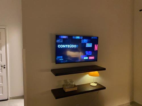 uma televisão de ecrã plano numa parede com um candeeiro em Casa Baronesa Suítes em São Sebastião