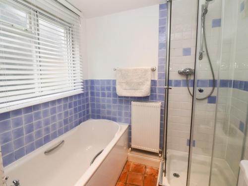 a blue tiled bathroom with a tub and a shower at Cobblers Cottage, Southwold in Southwold
