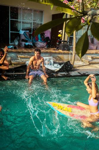 a man and a woman sitting on a surfboard in a swimming pool at LoTide Surf Camp Uluwatu in Uluwatu