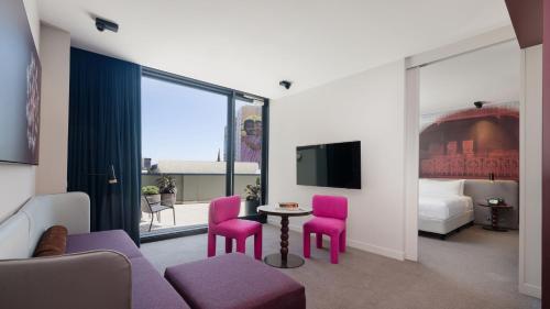 Cette chambre d'hôtel dispose de chaises roses, d'une table et d'une télévision. dans l'établissement Hotel Indigo Sydney Potts Point, an IHG Hotel, à Sydney