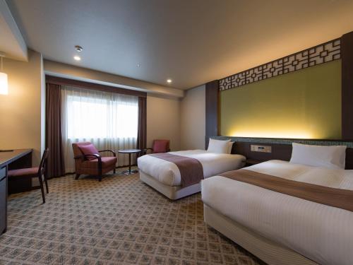 a hotel room with two beds and a desk at JR Kyushu Hotel Nagasaki in Nagasaki