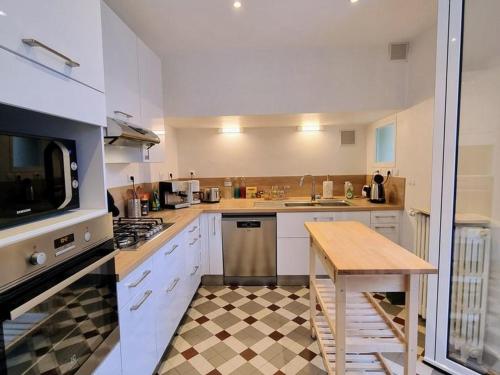 une cuisine avec des armoires blanches, une table et un micro-ondes dans l'établissement Maison de meulière près de Paris avec jardin, cheminée et tout confort inclus - FR-1-527-45, à Carrières-sur-Seine